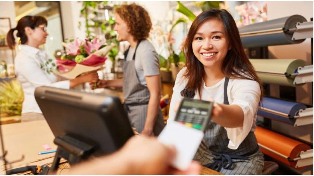 Young female cashier hands point of sale terminal to customer.